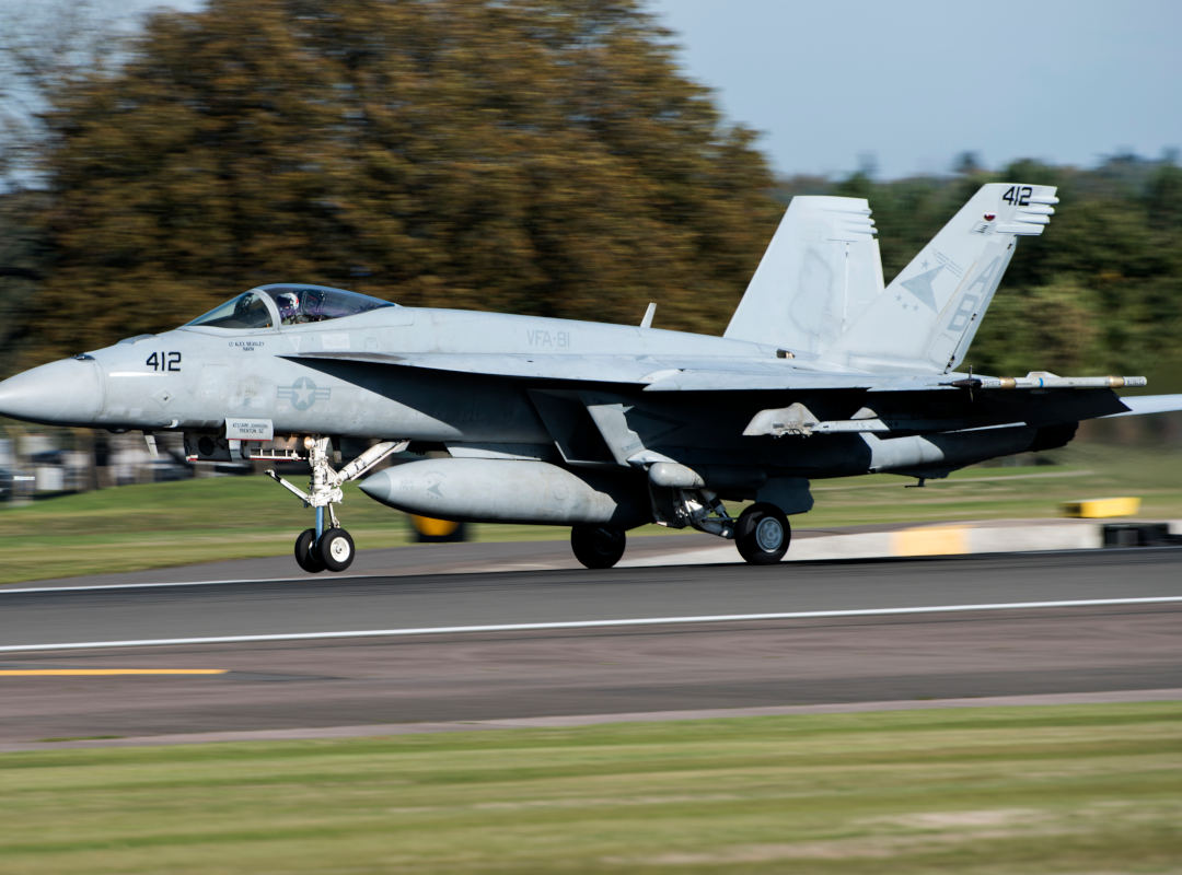 U.S. Navy F/A-18 Super Hornet, number 412, touching down on a runway with its landing gear extended.